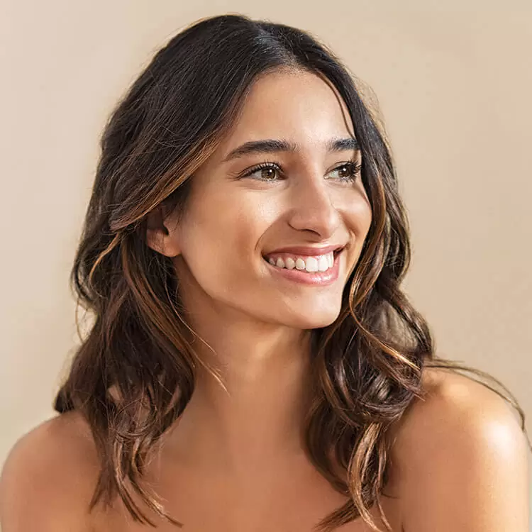 A smiling woman looking off-camera, imagining her future results after a complimentary smile consultation to discuss cosmetic dental improvements