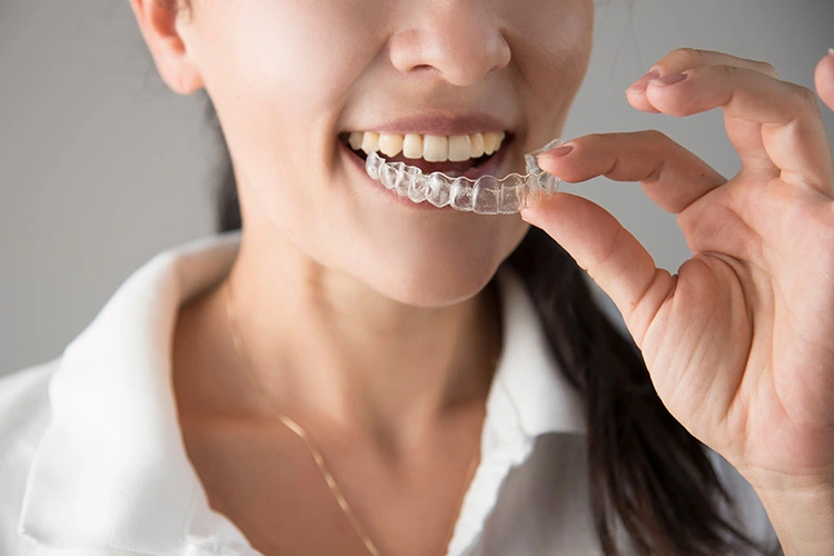 A woman smiles while holding a clear dental aligner near her teeth, conveying a sense of confidence and dental care