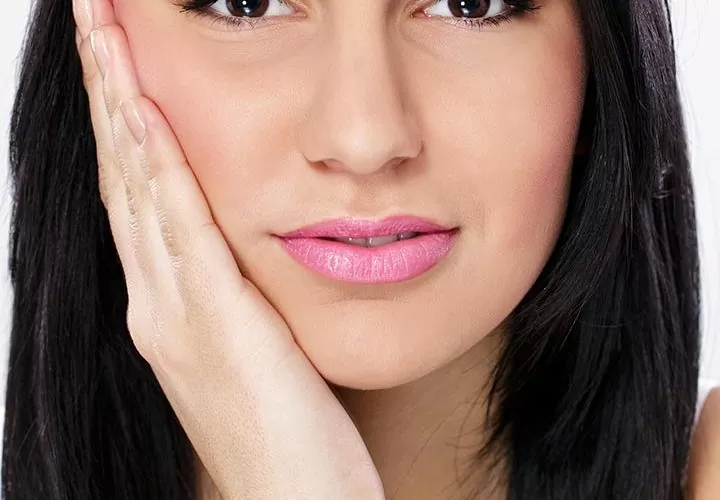 A close-up of a woman touching her jaw in discomfort, illustrating common symptoms of TMJ pain and the need for specialized neuromuscular dental treatment.