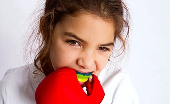 A young girl wearing red boxing gloves, smiling confidently while posing for the camera.
