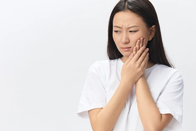 A woman touching her cheek appears in pain, suggesting toothache