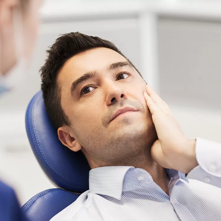 A man in a dental chair touches his cheek, appearing concerned or in discomfort