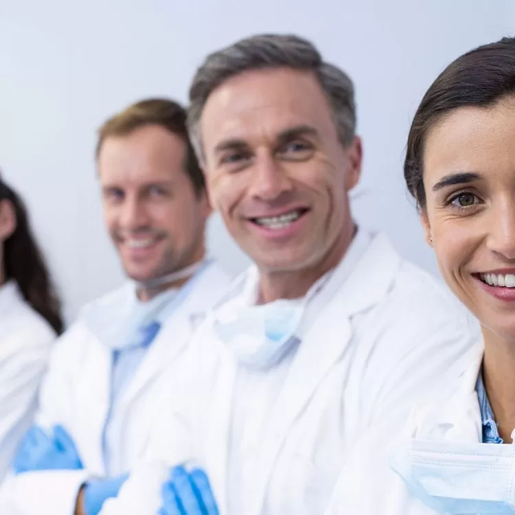 A group of smiling medical professionals in white lab coats and masks