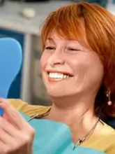 Smiling woman hand mirror in a dental clinic