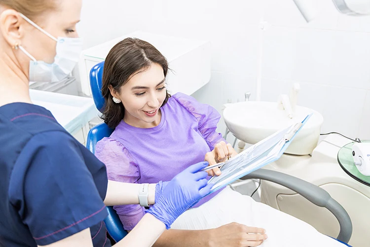 A woman sits in a dental chair, smiling and engaging with a dental professional