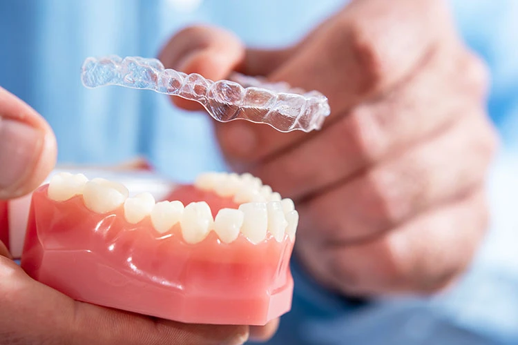 Person holding a dental model with teeth in one hand and a clear orthodontic aligner
