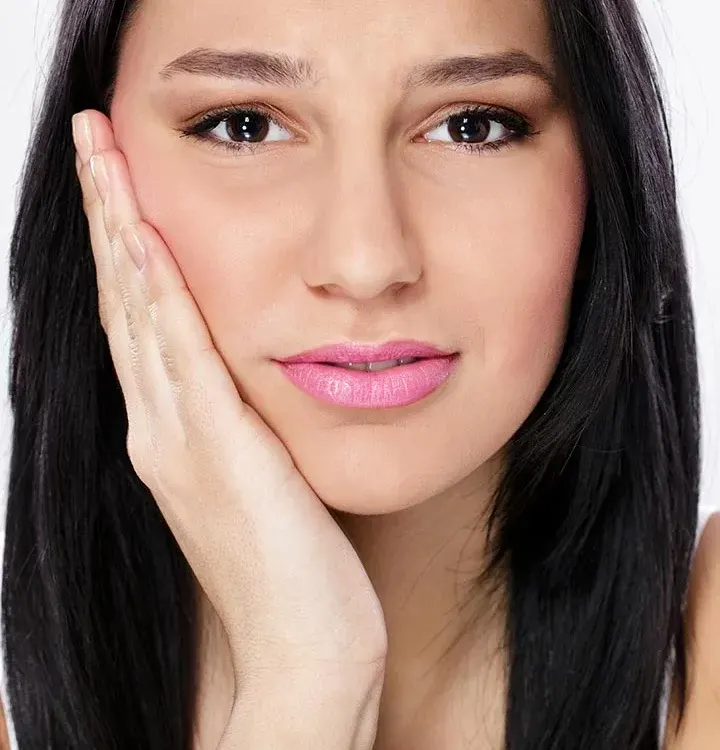 A woman with black hair touches her cheek, expressing discomfort or pain
